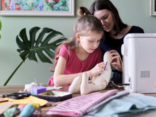 girl sews a doll with mom